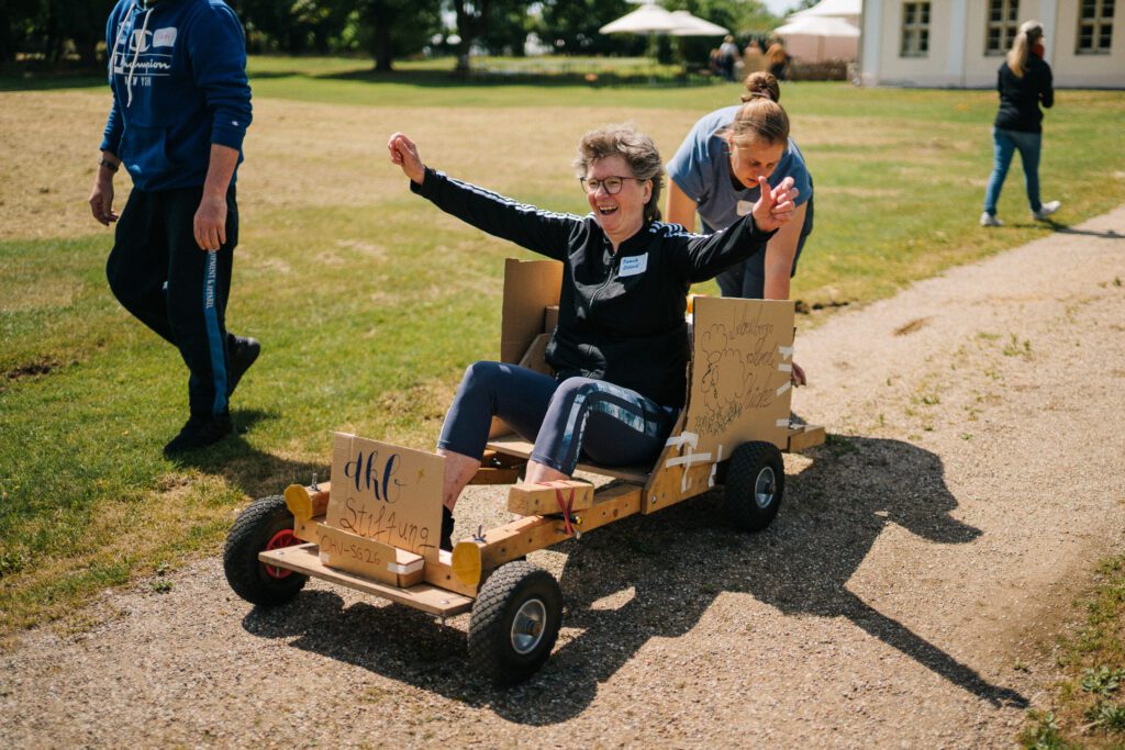 Zwei Mitarbeiterinnen der DKB STIFTUNG testen beim Teamtag 2026 ein selbst gebautes Fahrzeug – eine sitzt im Wagen, die andere schiebt ihn an.