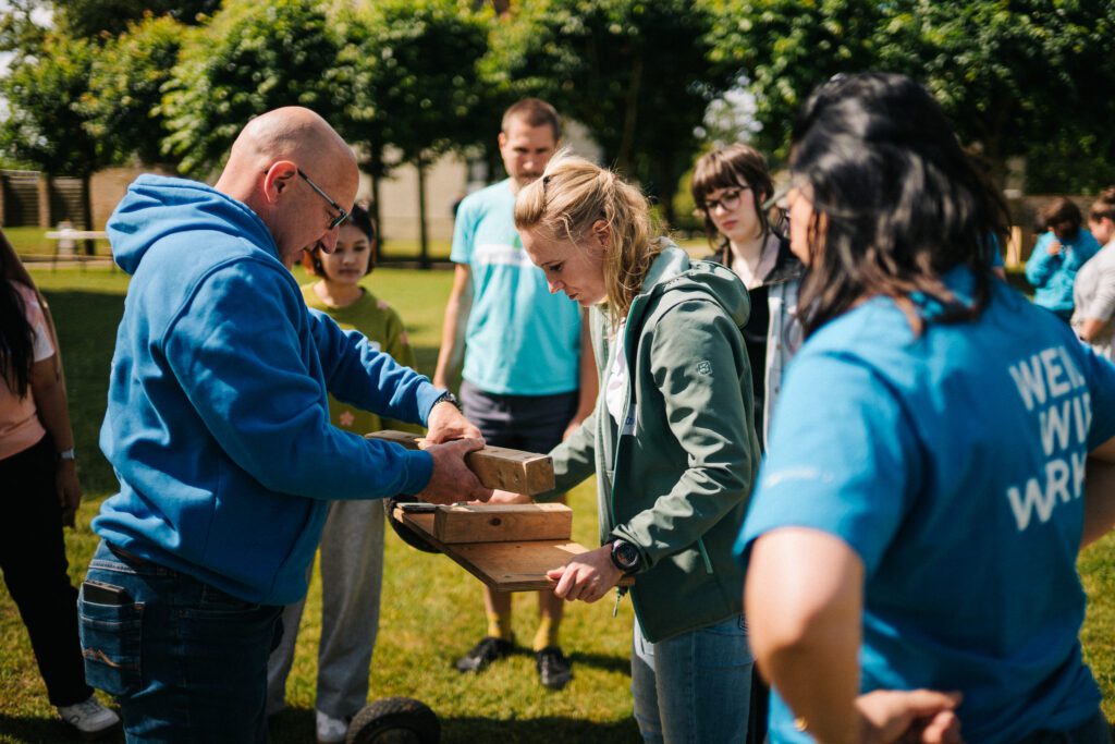 Mitarbeitende der DKB STIFTUNG arbeiten beim Teamtag 2026 gemeinsam an einer Teamaufgabe und prüfen, wie Holzteile zu einer Konstruktion zusammenpassen.