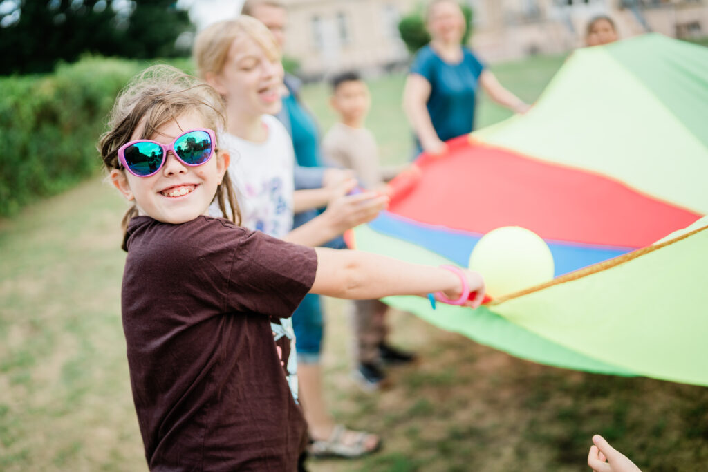 Kinder halten ein großes buntes Schwung-Tuch in den Händen und balancieren einen Ball darauf